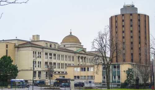 Historic building with a dome and modern cylindrical structure beside it, set against a cloudy sky.
