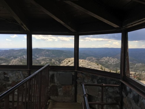View from inside a lookout tower, showcasing a panoramic landscape of mountains and valleys under a cloudy sky.