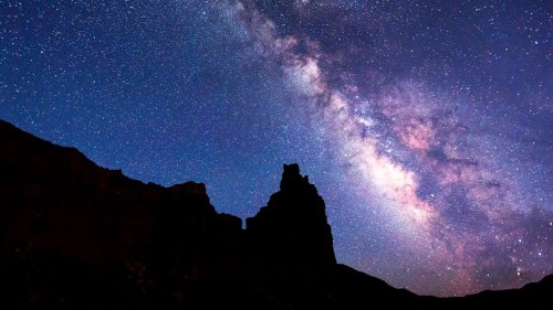 Silhouette of a rocky formation against a starry night sky with the Milky Way prominently displayed.