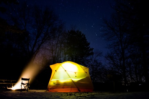 A glowing yellow tent under a starry night sky, with a camp chair and a beam of light illuminating the scene.