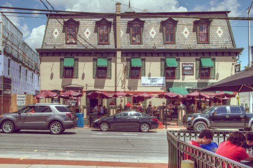 A historic building with green awnings and outdoor seating, bustling with patrons on a sunny day.