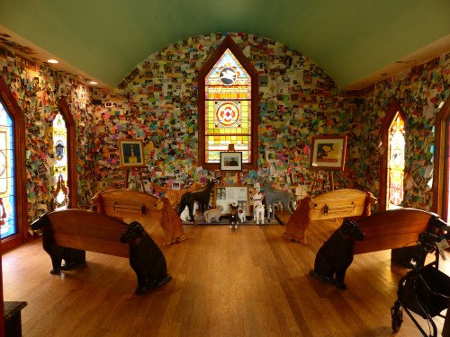 A colorful room with a wall covered in cards, featuring two wooden coffins and various dog sculptures.