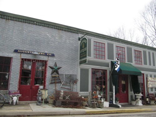 A vintage storefront with red windows, holiday lights, and various antiques displayed outside.