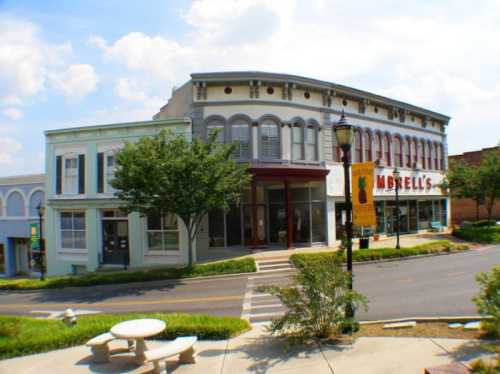 Historic buildings line a street, featuring a mix of architectural styles and greenery under a blue sky.