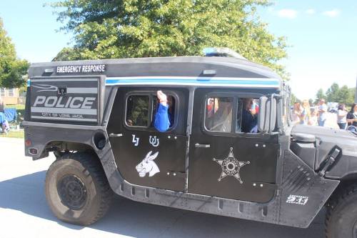 A police vehicle with emergency response markings drives past a crowd at an outdoor event.