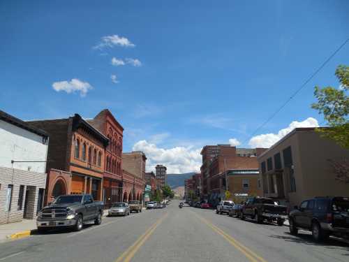 A wide street lined with historic buildings and parked cars under a blue sky with scattered clouds.