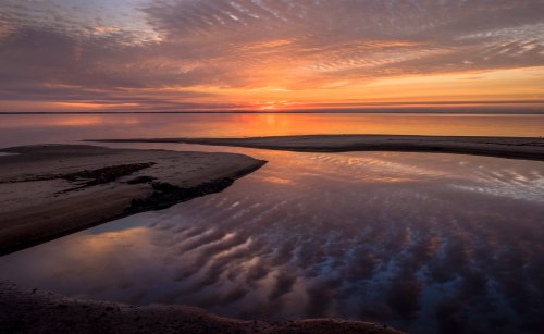 A serene sunset over calm waters, with vibrant colors reflecting on the surface and soft clouds in the sky.