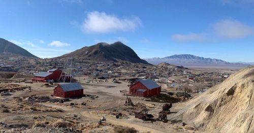 A panoramic view of a ghost town with red buildings, mountains, and a clear blue sky in the background.