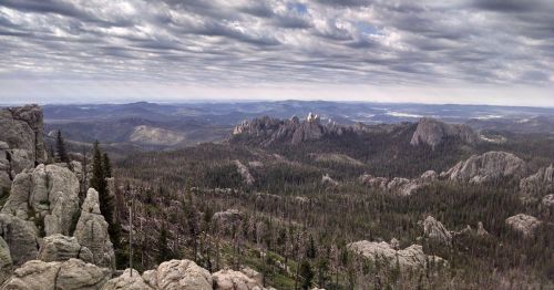 A panoramic view of rugged mountains and dense forests under a cloudy sky, showcasing natural beauty and vast landscapes.