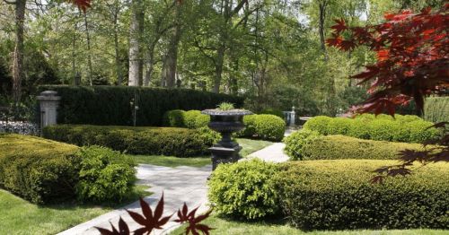Lush garden with neatly trimmed hedges, a stone pathway, and a decorative urn surrounded by greenery.