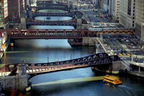 Aerial view of Chicago's bridges over the river, with a yellow boat and city buildings in the background.