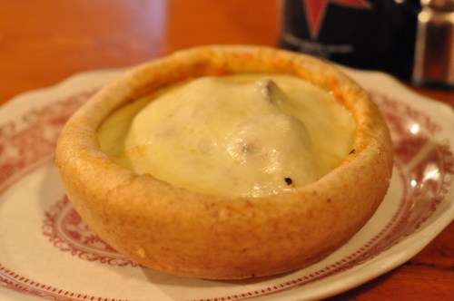 A cheesy dish served in a round, crusty bowl on a decorative plate.