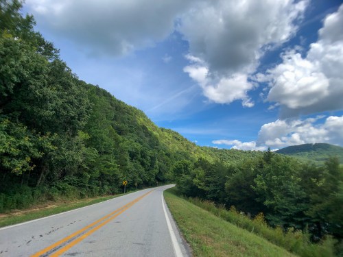 A winding road surrounded by lush green hills under a partly cloudy blue sky.