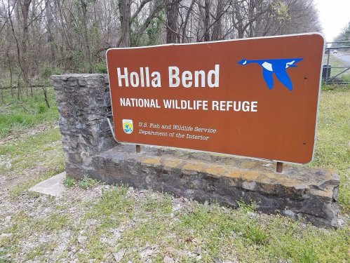 Sign for Holla Bend National Wildlife Refuge, featuring a blue bird graphic and information about the U.S. Fish and Wildlife Service.