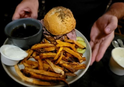 A plate with a sandwich, fries, a bowl of sauce, and a small cup of ranch dressing, held by a person.