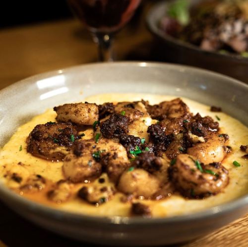 A bowl of creamy grits topped with seasoned shrimp and crispy bits, garnished with herbs.