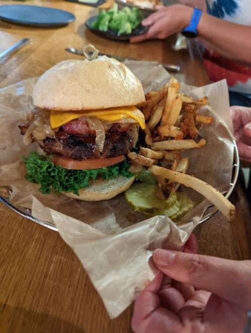 A close-up of a juicy burger with cheese, bacon, and onions, served with fries and pickles on a plate.