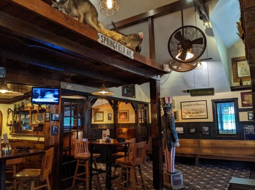 Cozy pub interior with wooden bar stools, vintage decor, a TV, and a statue of Uncle Sam near the restrooms sign.