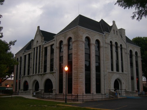 Historic stone building with large windows and decorative architecture, surrounded by trees and a lamppost.