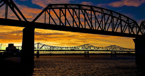 Silhouette of bridges against a vibrant sunset sky over water.