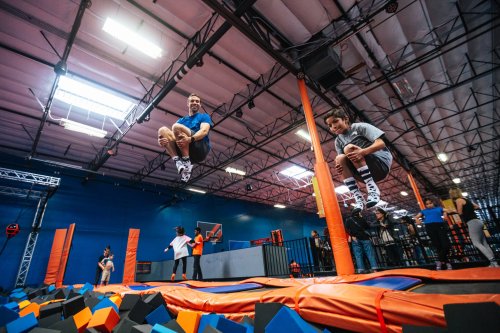 Two people jumping on trampolines above a foam pit in a vibrant indoor trampoline park.