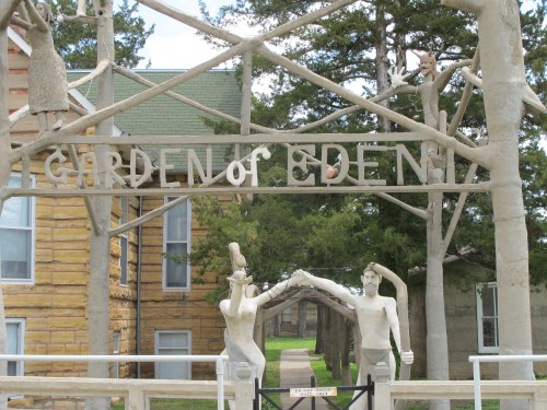 A stone archway reading "Garden of Eden" with sculptures of figures and trees in a park-like setting.