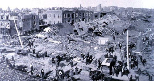 Historic photo of a devastated cityscape after a disaster, with collapsed buildings and crowds of people surveying the damage.