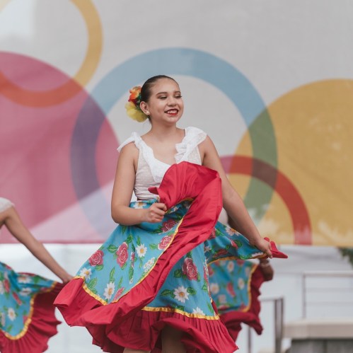A young dancer in a colorful floral dress twirls joyfully on stage, showcasing vibrant movement and expression.