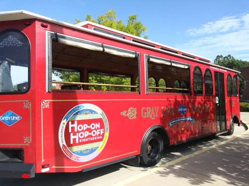 A red sightseeing trolley bus parked, featuring "Hop-On Hop-Off" signage and a decorative design.