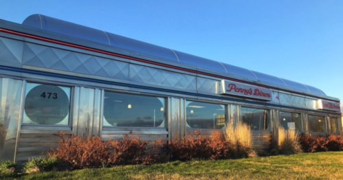 A shiny silver diner with large windows and a red sign reading "Penny's Diner," set against a clear blue sky.