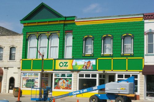 Colorful building with green and yellow exterior, featuring the "Oz Museum" sign and a lift parked outside.