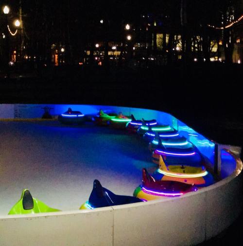 Colorful bumper cars illuminated by neon lights in a dark amusement park setting.
