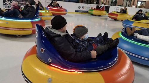 A man and a child enjoy a ride on colorful bumper cars at an indoor ice rink.