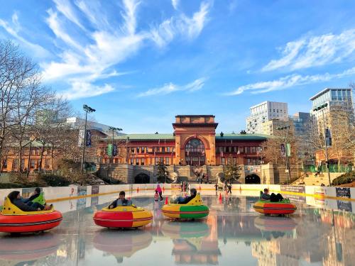 Colorful bumper cars on an ice rink with a historic building and blue sky in the background.
