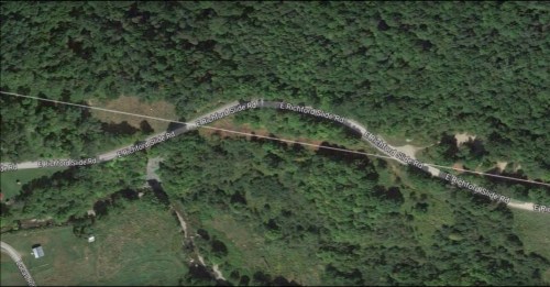 Aerial view of a winding road surrounded by dense green forest and open fields.