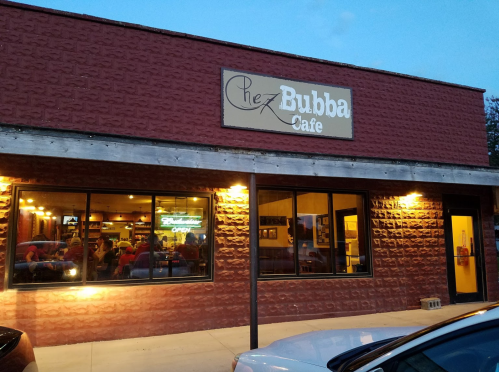 Exterior view of Chez Bubba Cafe, featuring a warm-lit entrance and a cozy atmosphere during dusk.