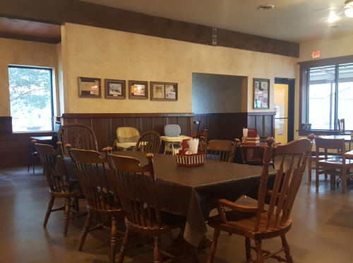 A cozy dining area with wooden tables and chairs, featuring framed pictures on the walls and a warm atmosphere.