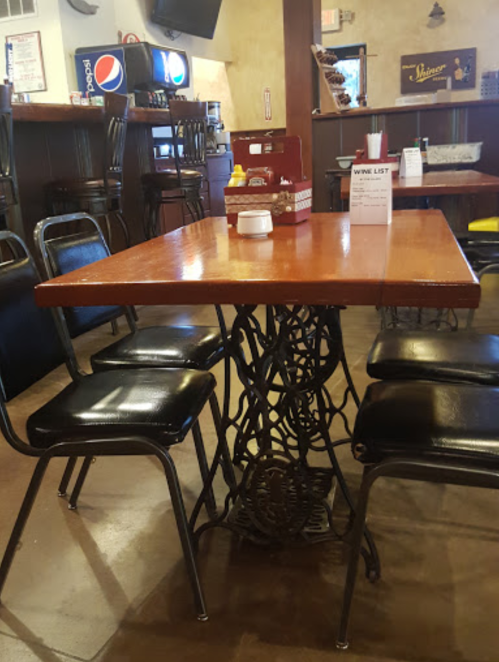 A wooden table with a decorative metal base surrounded by black chairs in a casual dining setting.