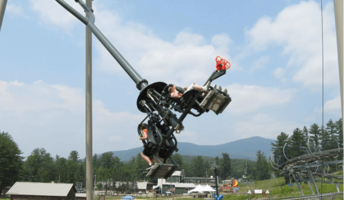 A thrilling amusement park ride spins upside down against a backdrop of mountains and trees.
