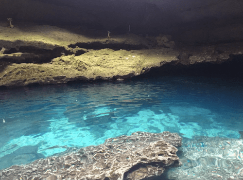A serene underground cave with clear blue water and rocky formations illuminated by soft light.