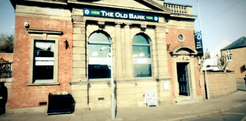 Historic building with a sign reading "The Old Bank," featuring brick architecture and large arched windows.