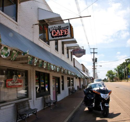 Exterior of White House Café with a motorcycle parked outside, featuring a sunny sky and decorative banners.