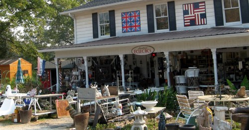 A charming antique shop with various outdoor decor and furniture, featuring colorful flags on the building.