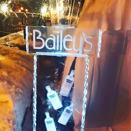 An ice sculpture sign for Bailey's, featuring bottles of whiskey, set against a snowy background.