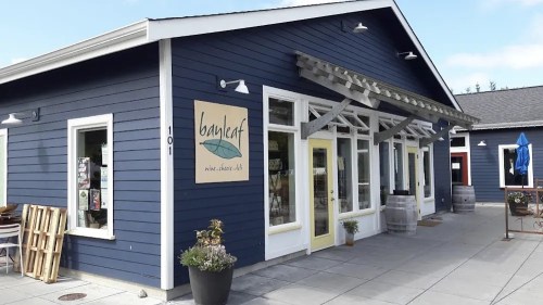 A blue building with a sign reading "bayleaf" and outdoor seating, surrounded by barrels and a patio area.