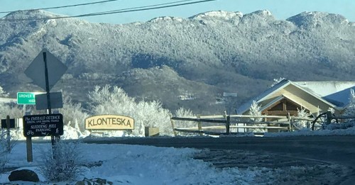 Snow-covered landscape with mountains in the background and a sign for Klonteska. Road signs visible nearby.