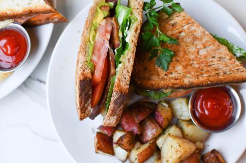 A toasted sandwich with lettuce and tomato, served with roasted potatoes and two small cups of ketchup.