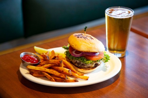 A juicy burger with lettuce, tomato, and onion, served with fries and ketchup, alongside a glass of beer.