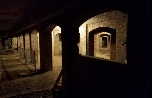 Dimly lit underground corridor with arched brick walls and scattered debris.
