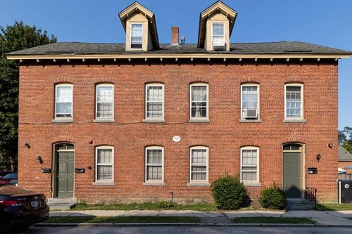 A red brick duplex with two stories, featuring gabled roofs and multiple windows on each side.